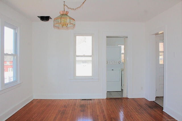 unfurnished room with hardwood / wood-style flooring, plenty of natural light, baseboards, and stacked washer and clothes dryer