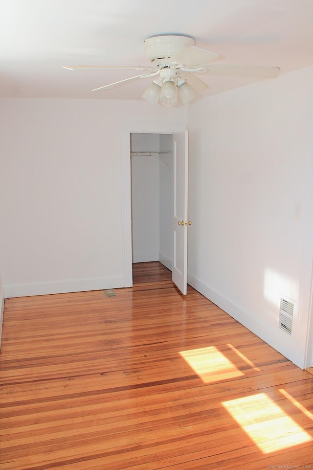 spare room with light wood-type flooring, ceiling fan, visible vents, and baseboards