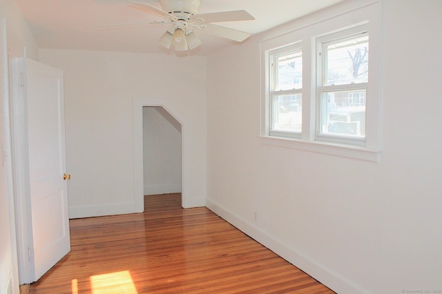 spare room featuring ceiling fan, light wood-type flooring, arched walkways, and baseboards