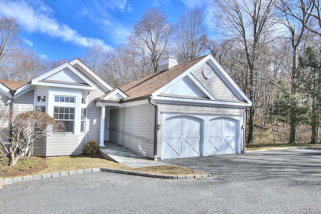 view of front of property featuring aphalt driveway, roof with shingles, a chimney, and an attached garage