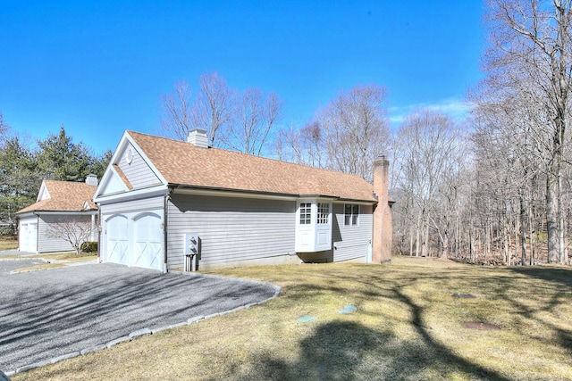 view of property exterior featuring a garage, a chimney, a yard, and roof with shingles