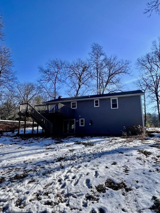 snow covered back of property featuring a deck and stairway