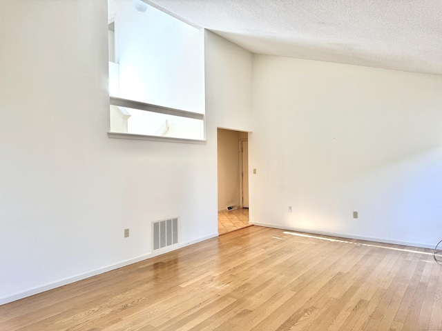 spare room with light wood-style floors, baseboards, visible vents, and a textured ceiling