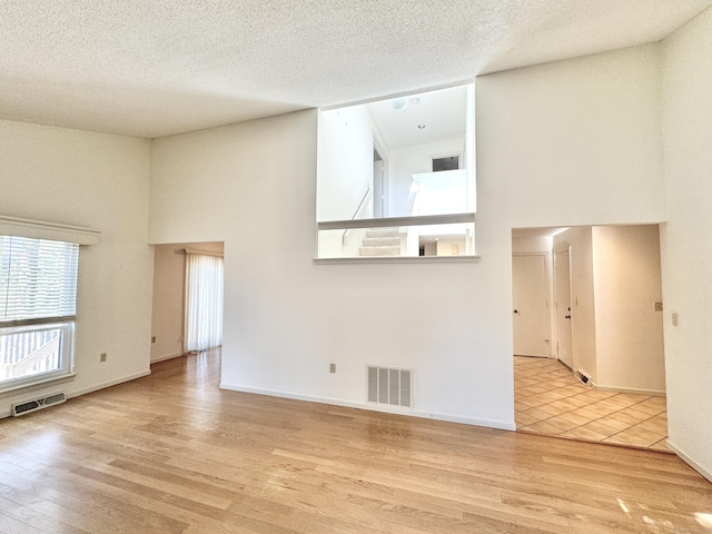 unfurnished living room with visible vents, a towering ceiling, and wood finished floors