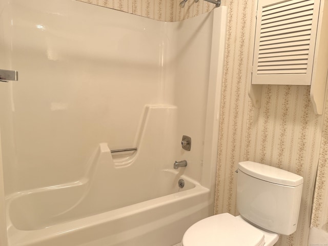 bathroom with toilet, wallpapered walls, and shower / washtub combination