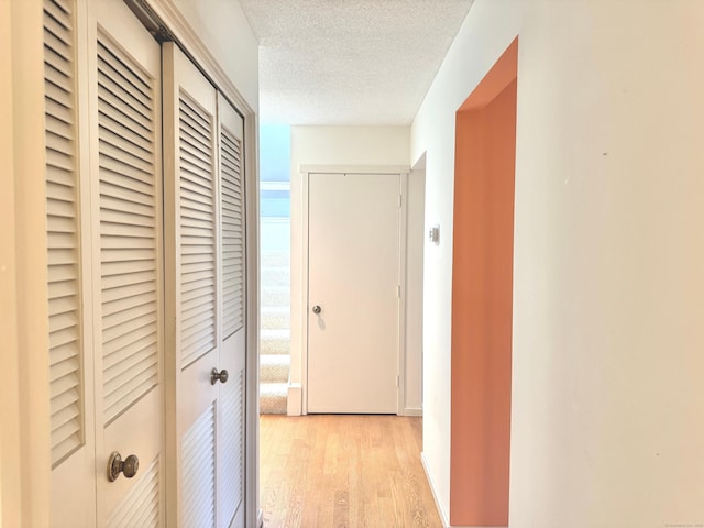 corridor featuring light wood-style flooring and a textured ceiling