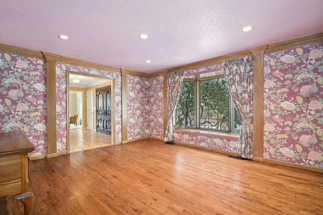 empty room featuring wood finished floors, crown molding, baseboards, and wallpapered walls