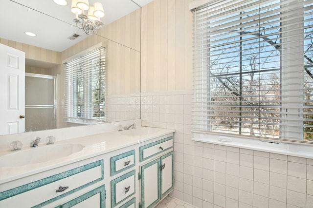 full bath featuring visible vents, a sink, tile walls, and double vanity