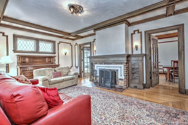 living room with coffered ceiling, wood finished floors, beamed ceiling, crown molding, and a brick fireplace