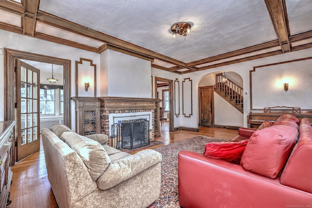 living room featuring arched walkways, coffered ceiling, wood-type flooring, a textured ceiling, and a fireplace