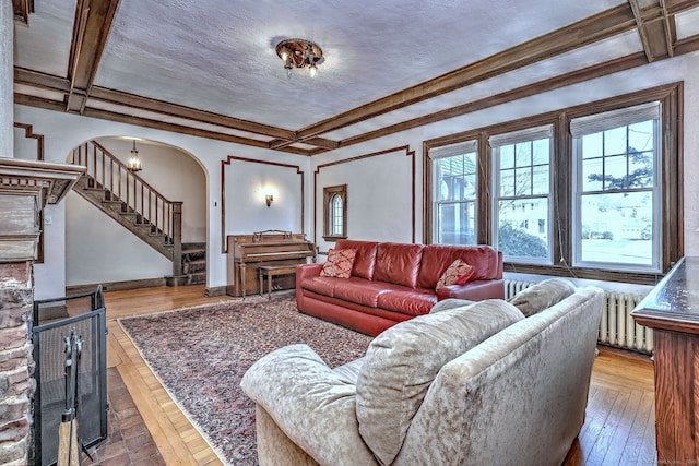 living area featuring stairs, arched walkways, coffered ceiling, and beam ceiling