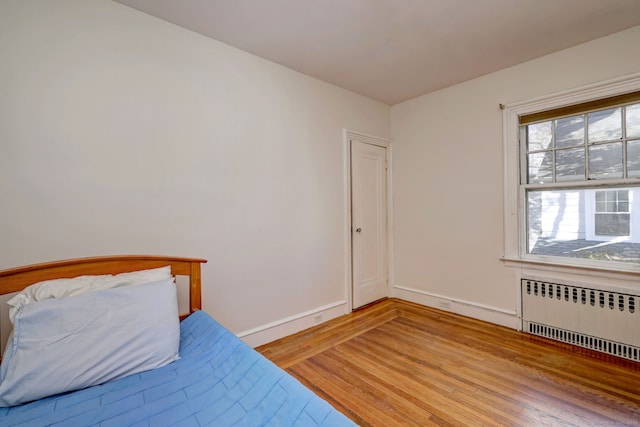 bedroom with radiator, light wood finished floors, and baseboards