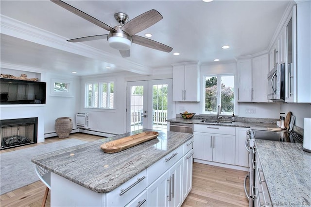 kitchen featuring light stone counters, a fireplace, stainless steel appliances, white cabinetry, and a sink