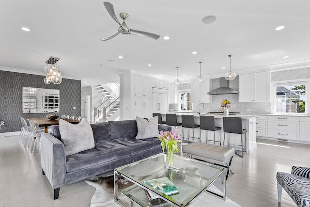 living area with ceiling fan with notable chandelier, recessed lighting, stairs, and crown molding