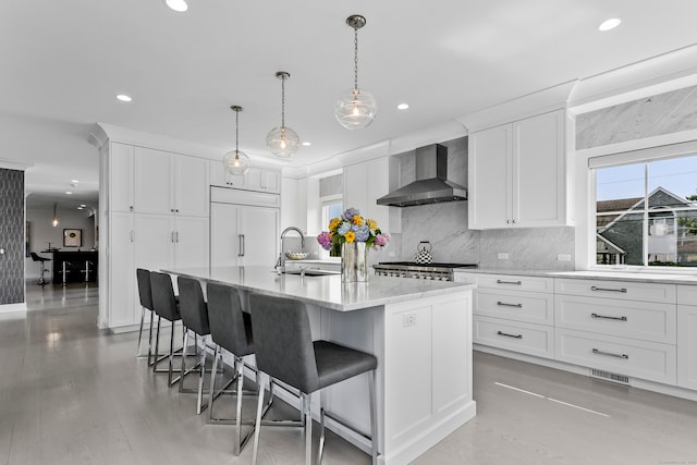 kitchen with wall chimney range hood, a kitchen breakfast bar, paneled built in refrigerator, a sink, and recessed lighting