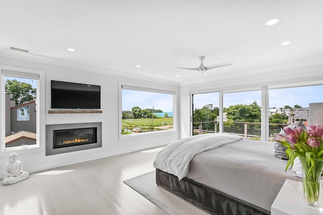 bedroom featuring a glass covered fireplace, wood finished floors, visible vents, and recessed lighting