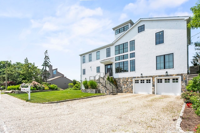 view of front of home with an attached garage, driveway, stone siding, and a front lawn