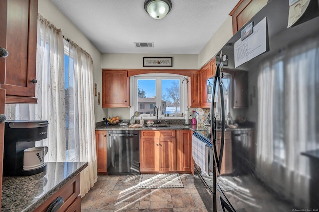 kitchen featuring visible vents, dark stone countertops, stone finish flooring, black appliances, and a sink