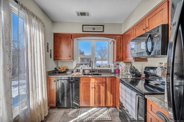 kitchen featuring brown cabinetry, visible vents, a sink, and black appliances