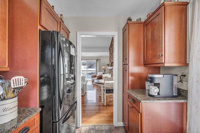 kitchen featuring light stone counters, brown cabinetry, wood finished floors, and freestanding refrigerator