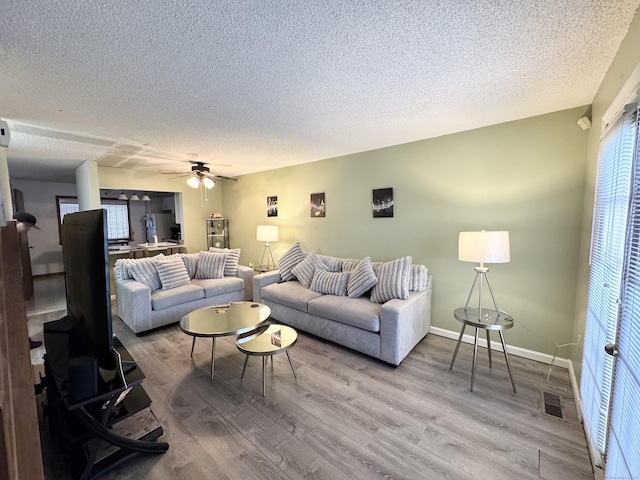 living area featuring a textured ceiling, wood finished floors, a ceiling fan, and baseboards