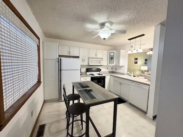 kitchen featuring visible vents, a ceiling fan, white cabinets, a sink, and white appliances