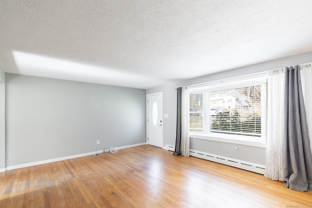 unfurnished room featuring a textured ceiling, baseboard heating, wood finished floors, and baseboards