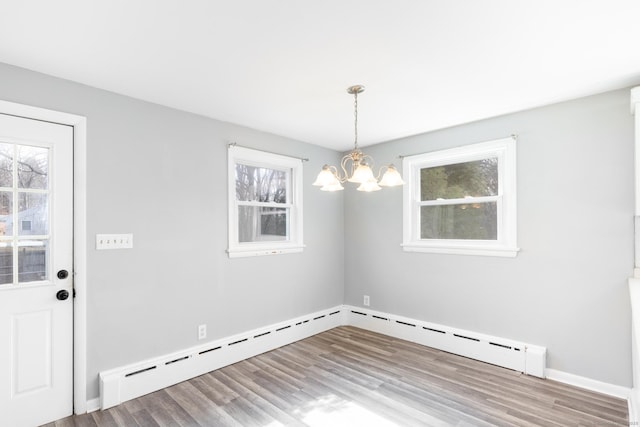 unfurnished dining area featuring baseboard heating, wood finished floors, a wealth of natural light, and a notable chandelier