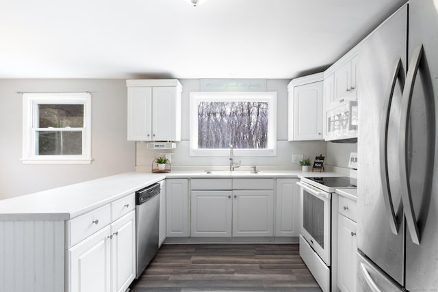 kitchen with dark wood finished floors, a peninsula, stainless steel appliances, white cabinetry, and a sink