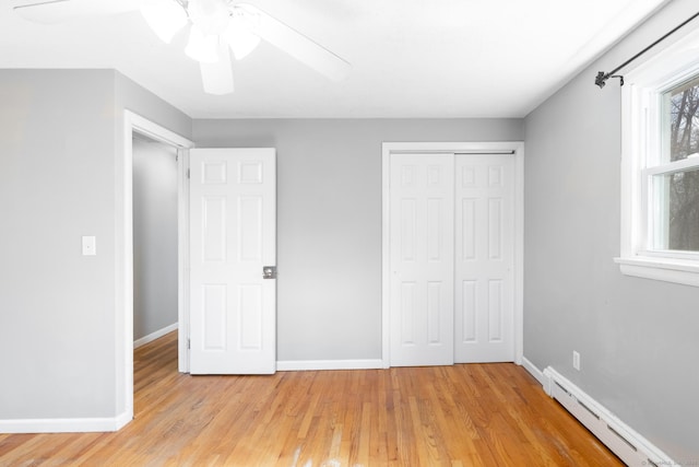 unfurnished bedroom featuring a baseboard radiator, a closet, light wood-style flooring, and baseboards