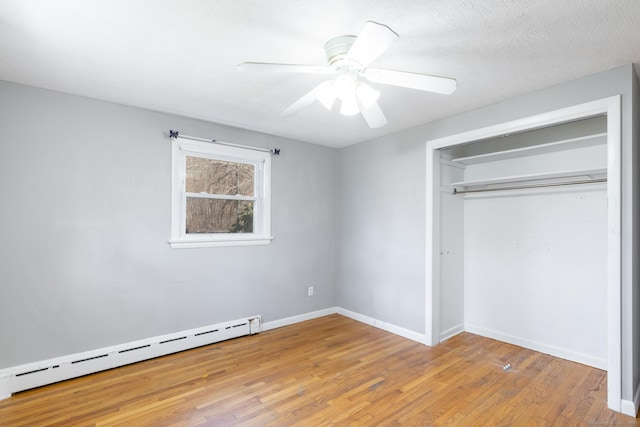 unfurnished bedroom featuring a baseboard radiator, a closet, ceiling fan, wood finished floors, and baseboards