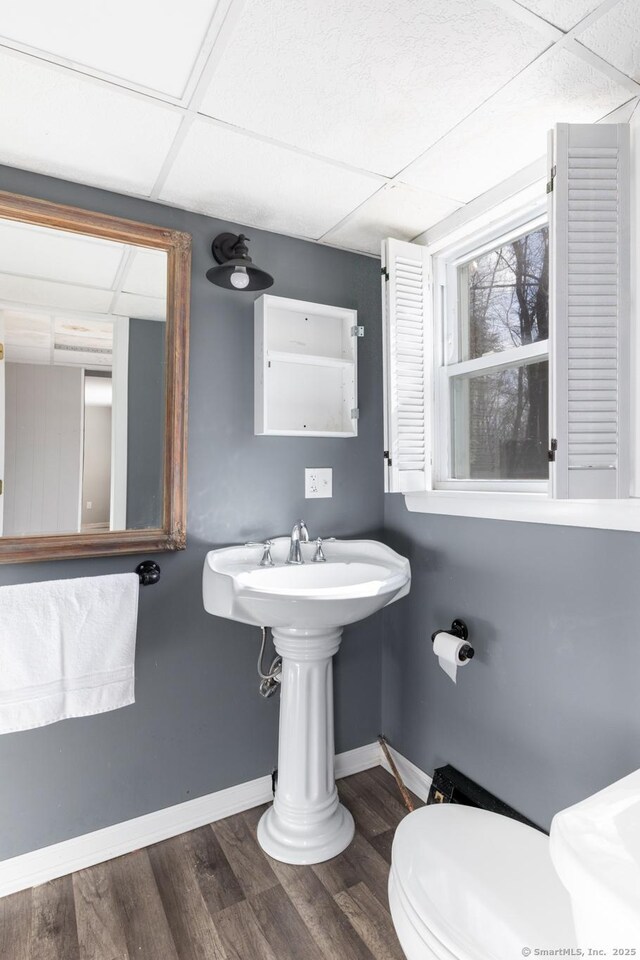 bathroom featuring a paneled ceiling, toilet, baseboards, and wood finished floors