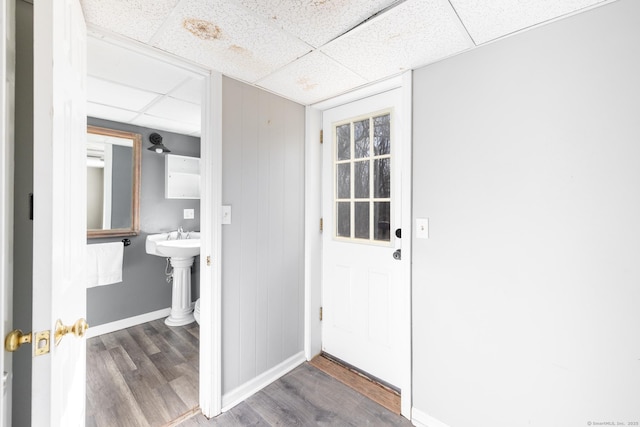 doorway with a sink, baseboards, a drop ceiling, and wood finished floors