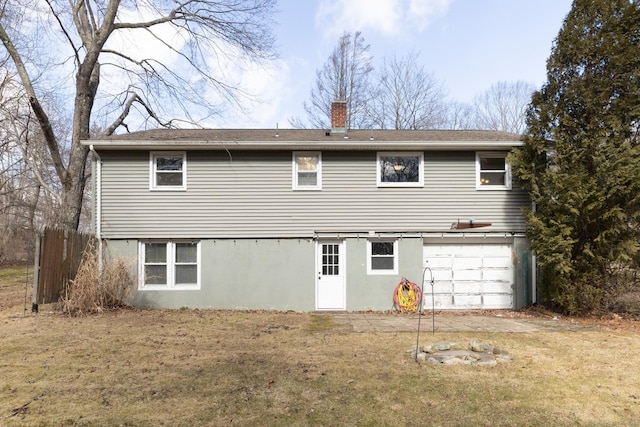 back of property with a chimney, an attached garage, and a lawn