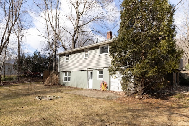 rear view of house featuring driveway, a lawn, and a chimney