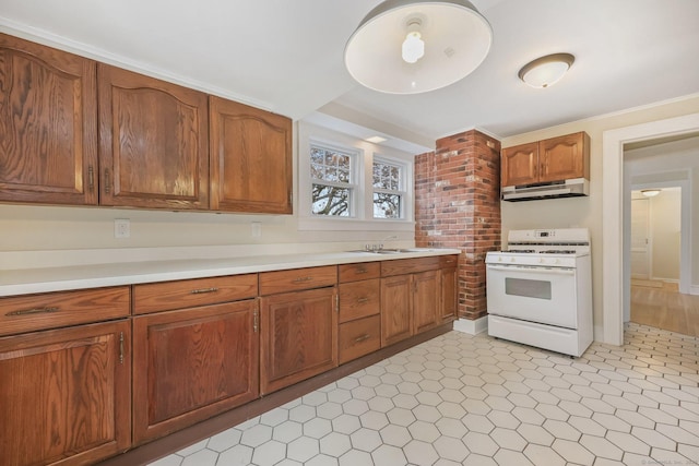 kitchen featuring white range with gas cooktop, brown cabinetry, light countertops, under cabinet range hood, and a sink