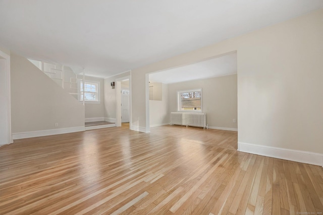 unfurnished living room featuring a wealth of natural light, light wood-type flooring, radiator, and baseboards