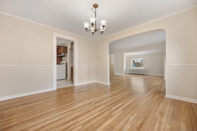 empty room with arched walkways, light wood-style flooring, a wainscoted wall, radiator heating unit, and washer / dryer