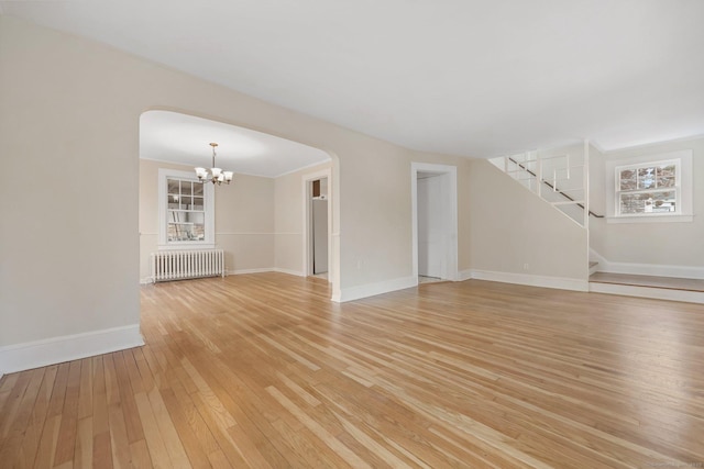 unfurnished living room with radiator, an inviting chandelier, light wood-style floors, baseboards, and stairs