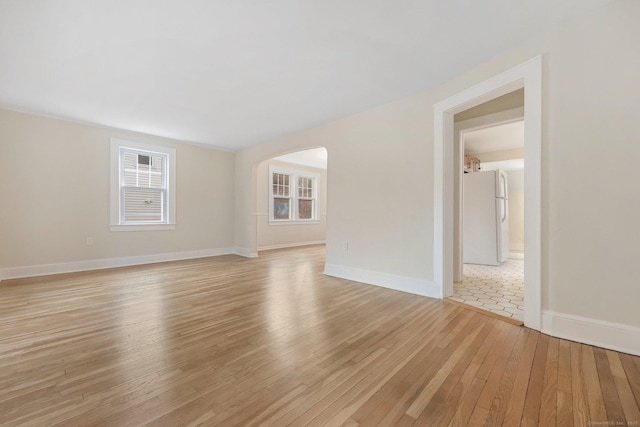 spare room with light wood-style floors, arched walkways, and baseboards