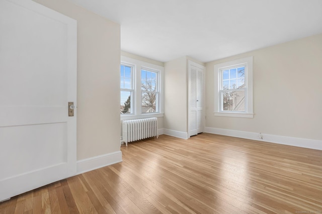 unfurnished bedroom with radiator, light wood-style flooring, and baseboards