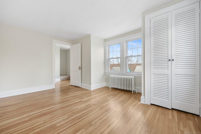 unfurnished bedroom with radiator, light wood-style flooring, baseboards, and a closet