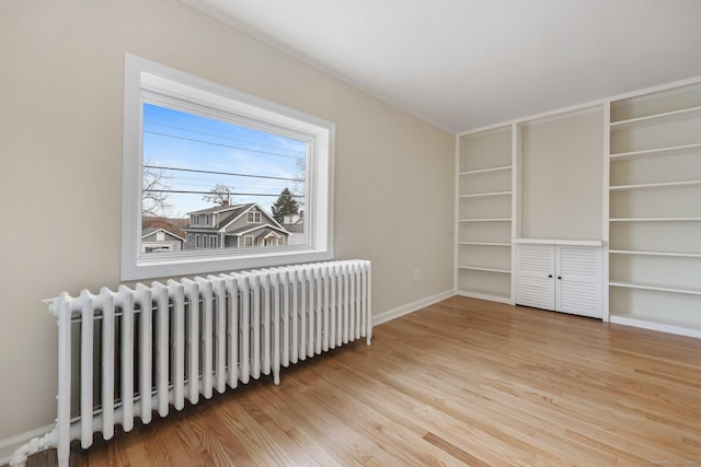 empty room with radiator heating unit, baseboards, and wood finished floors