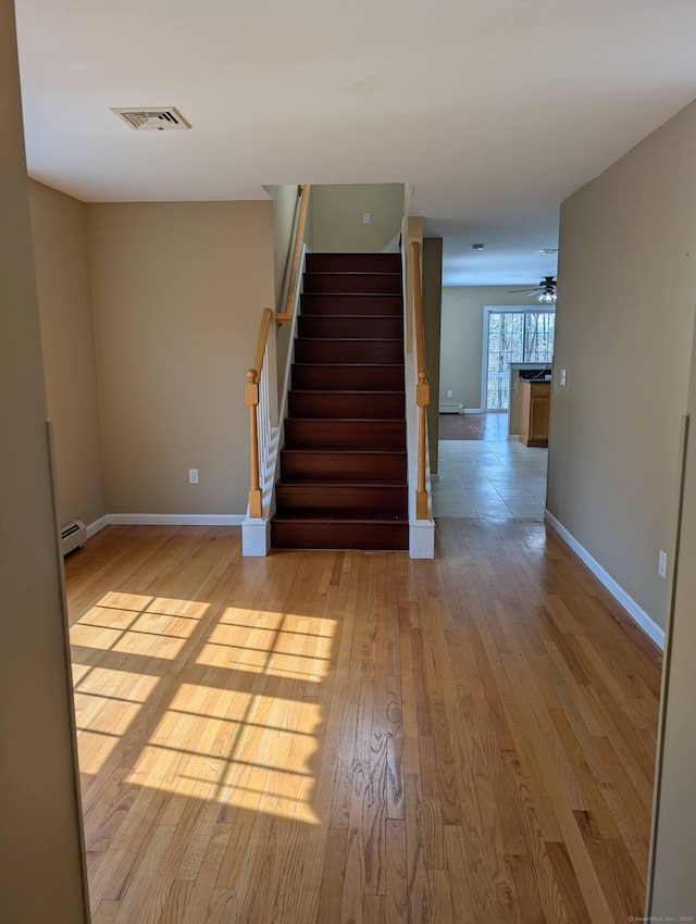 stairway with ceiling fan, a baseboard radiator, wood finished floors, visible vents, and baseboards