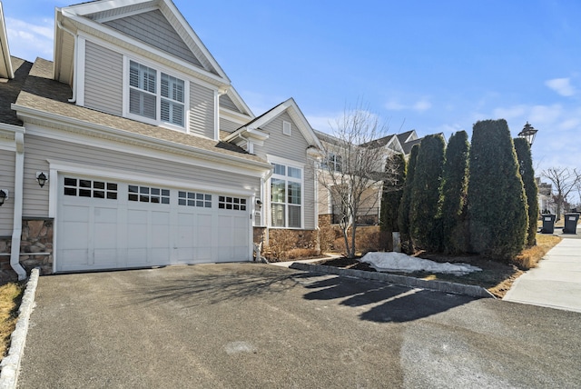 view of front of house featuring aphalt driveway, stone siding, roof with shingles, and a garage