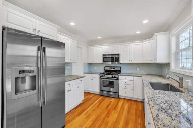 kitchen featuring appliances with stainless steel finishes, white cabinetry, a sink, and ornamental molding