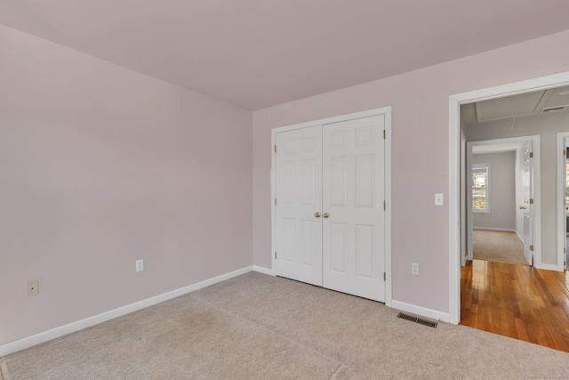 unfurnished bedroom with carpet floors, a closet, visible vents, attic access, and baseboards