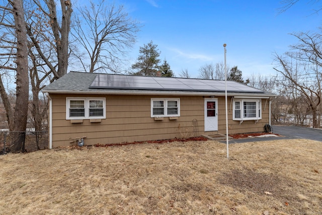 view of front of property with solar panels, roof with shingles, a front yard, and fence