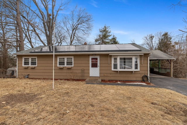 view of front of home with aphalt driveway, a front yard, a carport, and solar panels