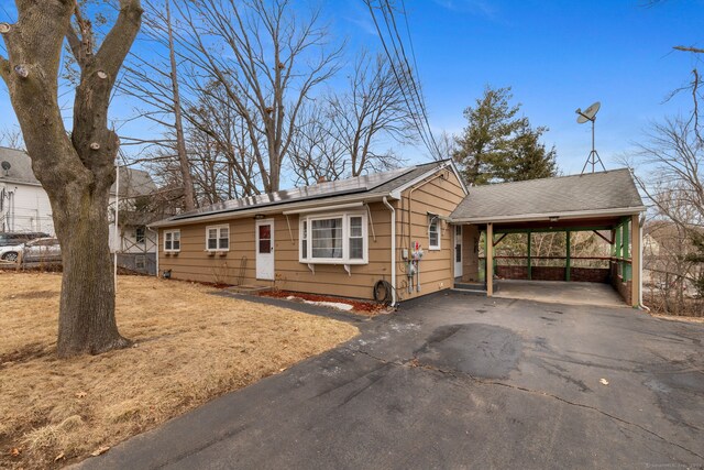 view of front of house with driveway, a shingled roof, roof mounted solar panels, and a carport